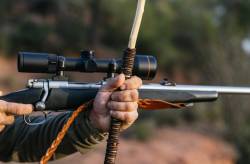 Detalle de rifle de caza estabilizado sobre un apoyo de palo artesanal durante un rececho.